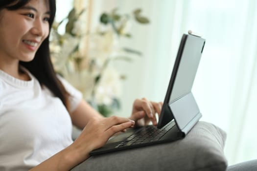 Smiling young woman in casual clothes browsing internet on digital tablet at home.