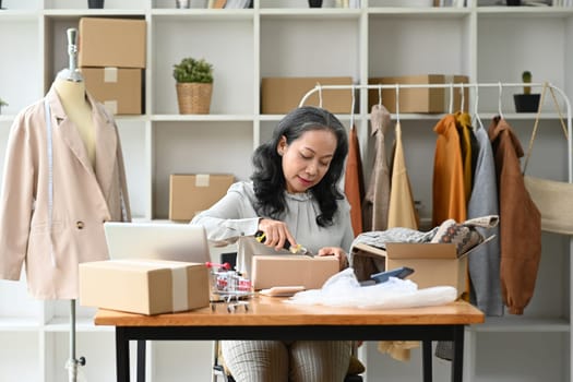 Small business owner packing clothes in a cardboard box for delivery to customers.