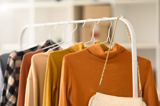 Different winter sweaters hanging on rack at designer clothes store. Clothing retails concept.