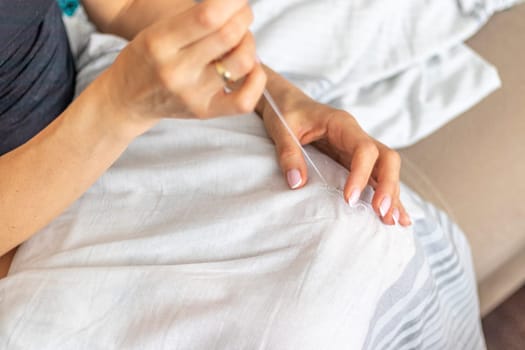 Shot of the woman with beautiful hands stitching up or patching a linen fabric