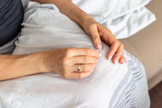 Shot of the woman with beautiful hands stitching up or patching a linen fabric