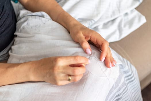 Shot of the woman with beautiful hands stitching up or patching a linen fabric