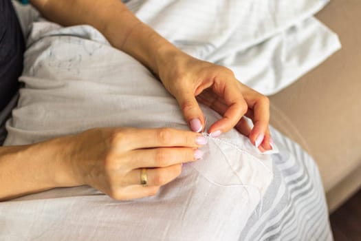 Shot of the woman with beautiful hands stitching up or patching a linen fabric