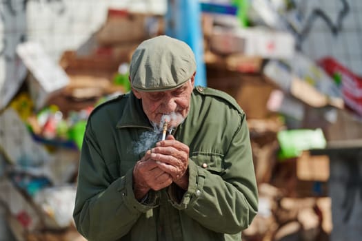 An elderly man is captured smoking a cigarette while wearing a dark green jacket and cap, exuding a sense of timeless style and sophistication.