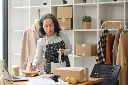 Middle age lady business owner working at her designer studio preparing parcel for shipping to customers.