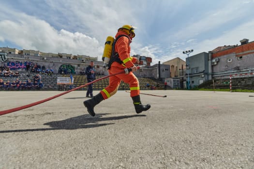 In a dynamic display of synchronized teamwork, firefighters hustle to carry, connect, and deploy firefighting hoses with precision, showcasing their intensive training and readiness for challenging and high-risk situations ahead.