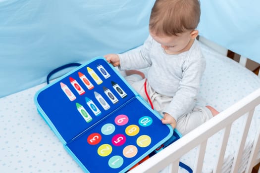 Little baby girl playing with busy book while sitting in crib. Concept of smart quiet books and modern educational toys