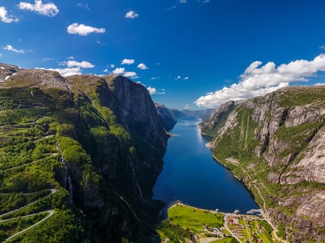 A breathtaking aerial view of a winding road snaking through a majestic fjord in Norway, with towering cliffs and lush green vegetation. Lysefjord, Norway