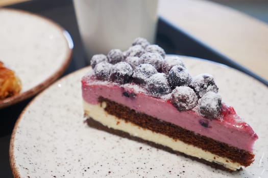 A delectable slice of berry cheesecake topped with blueberries and dusted with icing sugar on a plate.