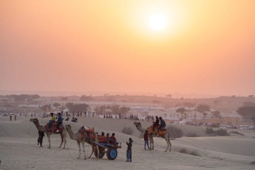 line of camels carrying people tourists at sunset across thar desert in jaisalmer rajasthan showing a popular tourist activity India