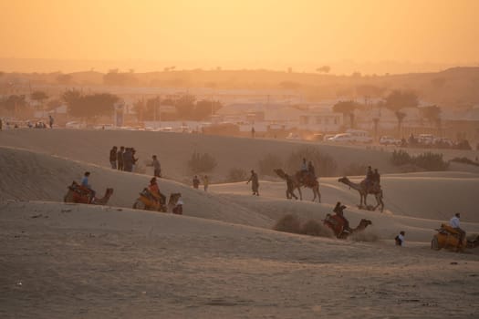 line of camels carrying people tourists at sunset across thar desert in jaisalmer rajasthan showing a popular tourist activity India