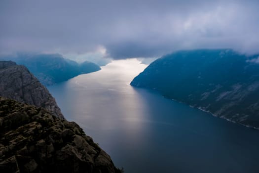 An aerial shot of a fjord in Norway, with a misty sky and mountains on either side of the water. Preikestolen, Norway