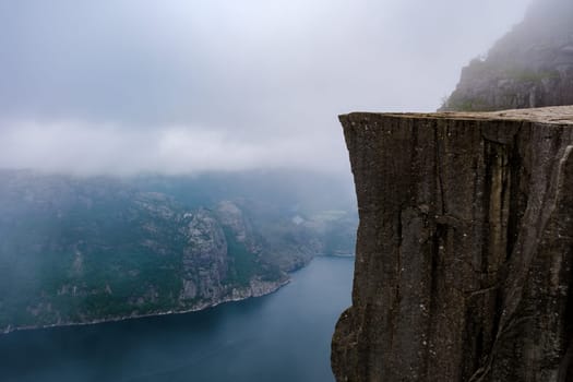 Preikestolen, Norway A breathtaking view of a towering cliff overlooking a fjord in Norway, with a misty, ethereal atmosphere.