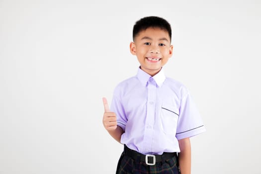 Portrait smile Asian little boy primary posing giving a thumbs up studio isolated white background, happy cute man kid wear school uniform plaid is expressing his approval, back to school concept