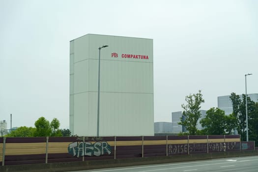 Ghent, Belgium - May 22, 2023: A white building with PBB CompacTuna signage in red letters, situated in an urban landscape. The building appears to be industrial, with a fence and trees in the foreground.