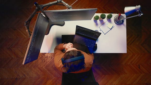 Top down view of developer typing complex code in home office, listening music and developing software application. IT expert wearing headphones, solving coding project tasks on laptop, aerial shot