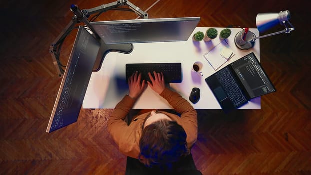 Top down view of remote worker typing code in personal office, using javascript language to develop software application. It specialist using multimonitor desktop setup to finish project, aerial shot