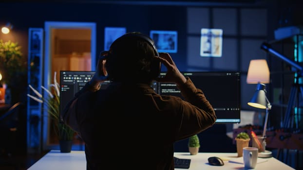 Engineer wearing headphones while using coding to fortify security, remotely working for IT company. Software expert listening music and upgrading binary code scripts on computer, camera B