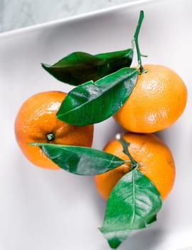 Tangerines with leaves on plate - citrus fruits and healthy eating flatlay styled concept