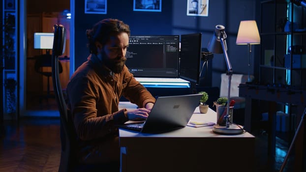 Computer scientist putting headphones on while developing code on PC, making time pass faster during remote job shift. IT admin doing multitasking in home office while listening music, camera B