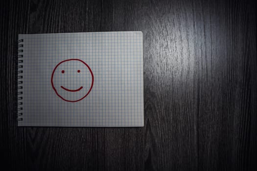 Smiley drawn on a notepad. Wooden table with notepad. High quality photo