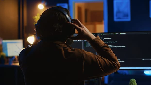 Engineer wearing headphones while using coding to fortify security, remotely working for IT company. Software expert listening music and upgrading binary code scripts on computer, camera A
