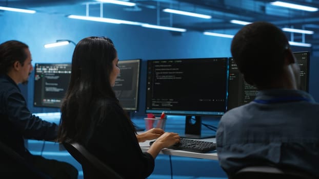 Multiethnic team of engineers working in high tech server hub, using PCs to analyze data. Multiracial group of employees examining infrastructure in data center, ensuring system integrity and security
