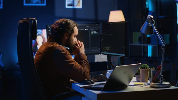 Technician focused on typing complex code in neon lit home office, developing software application. It specialist removing headphones to better concentrate on difficult task, camera A