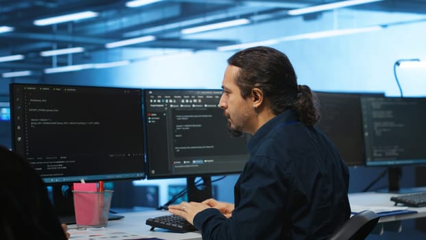 Knowledgeable engineer upgrading equipment in data center, zoom in shot. Specialist at PC desk in high tech establishment overseeing server rows, typing on keyboard, close up shot