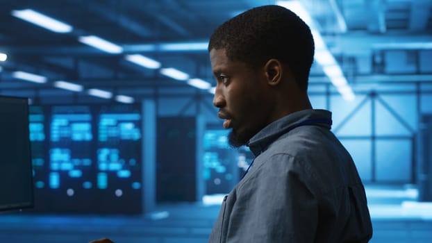 African american man working in server hub capable of processing vast amounts of data. IT programmer at PC desk typing on keyboard, updating servers controlling network resources, close up shot