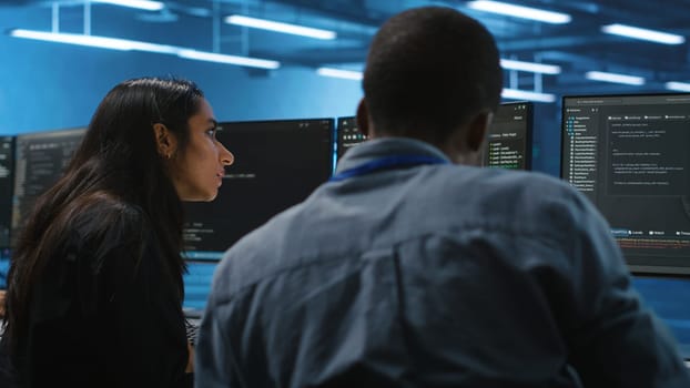 Diverse IT engineers in server room brainstorming ways to fix equipment storing datasets. Multiethnic coworkers discussing how to mend data center racks doing complex computational operations