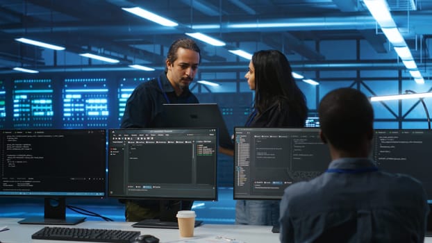 Multiethnic team of admins working in high tech server room capable of storing vast amounts of data. Diverse colleagues doing brainstorming, discussing ways to fix servers