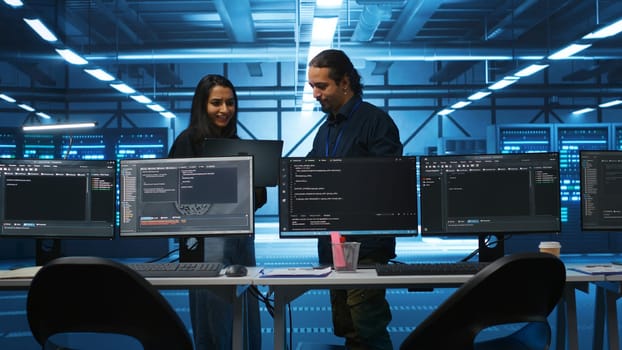 Multiracial colleagues in server hub workspace collaborating to fix servers providing computing resources for workloads. Engineers doing brainstorming while supervising data center supercomputers