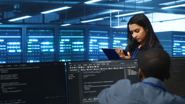 Manager overseeing server room, walking around with checklist on notepad, troubleshooting hardware. Supervisor doing inspection in server hub, monitoring energy consumption across rigs