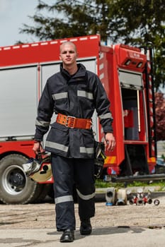 A firefighter, adorned in professional gear, stands confidently beside a fire truck following a grueling firefighting training session