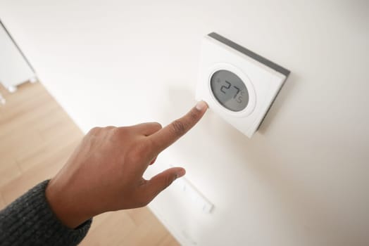 Hand adjusting smart home thermostat on white wall, displaying modern technology and interior system