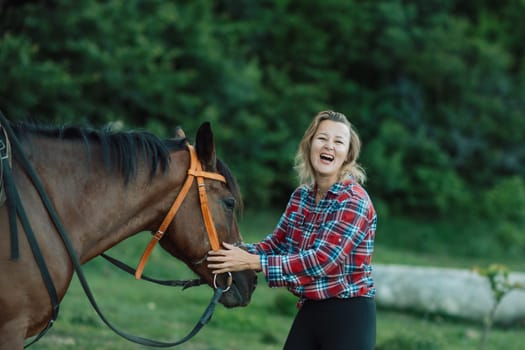 Happy blonde with horse in forest. Woman and a horse walking through the field during the day. Dressed in a plaid shirt and black leggings