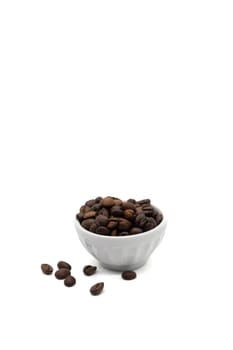 A white bowl filled with roasted coffee beans, with some of the beans scattered on the ground in front of it