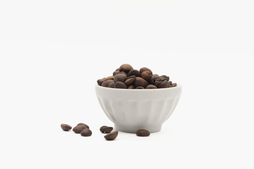 A white bowl filled with roasted coffee beans, with some of the beans scattered on the ground in front of it