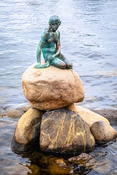 Copenhagen, Denmark, August 29 2023: Little mermaid statue displayed on a rock by the waterside at the Langelinie promenade in Copenhagen, Denmark, capital of Denmark. Statue was made in bronze by Edvard Eriksen in 1909
