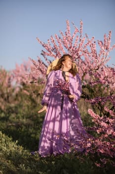 Woman blooming peach orchard. Against the backdrop of a picturesque peach orchard, a woman in a long pink dress and hat enjoys a peaceful walk in the park, surrounded by the beauty of nature