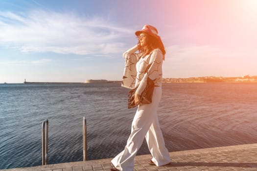 Stylish seashore woman. Fashionable woman in a hat, white trousers and a light sweater with a black pattern on the background of the sea