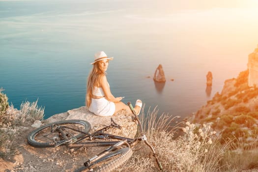 A woman cyclist on a mountain bike looking at the landscape of mountains and sea. Adventure travel on bike