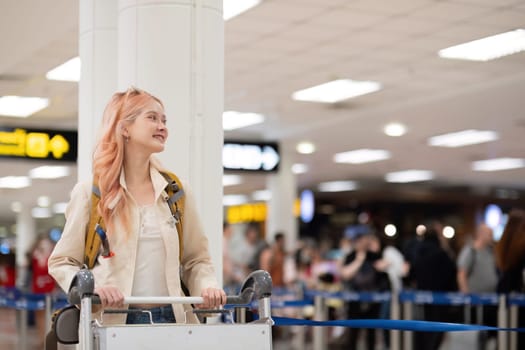 Young traveler with luggage cart and backpack at airport terminal. Concept of travel, exploration, and excitement.