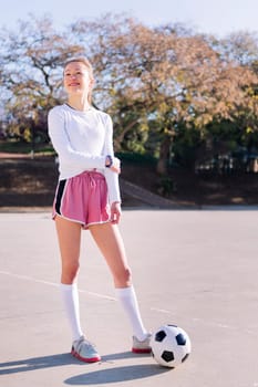 smiling young caucasian woman next to a soccer ball ready to play in a urban football court, concept of sport and active lifestyle