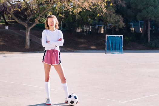 smiling young caucasian woman next to a soccer ball ready to play in a urban football court, concept of sport and active lifestyle, copy space for text