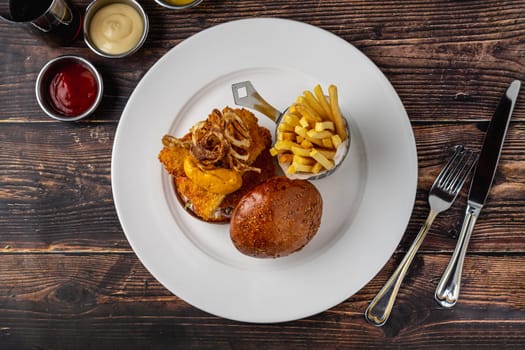 Chicken burger served with fries and sauces on a white porcelain plate