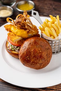 Chicken burger served with fries and sauces on a white porcelain plate