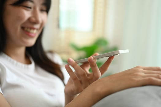 Smiling young woman in casual clothes enjoying pleasant mobile conversation in living room.