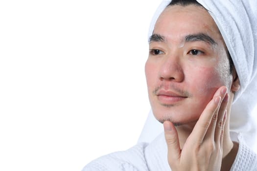 Young man in bathrobe applying moisturizer on his face carefully for rapid recovery after laser skin resurfacing.